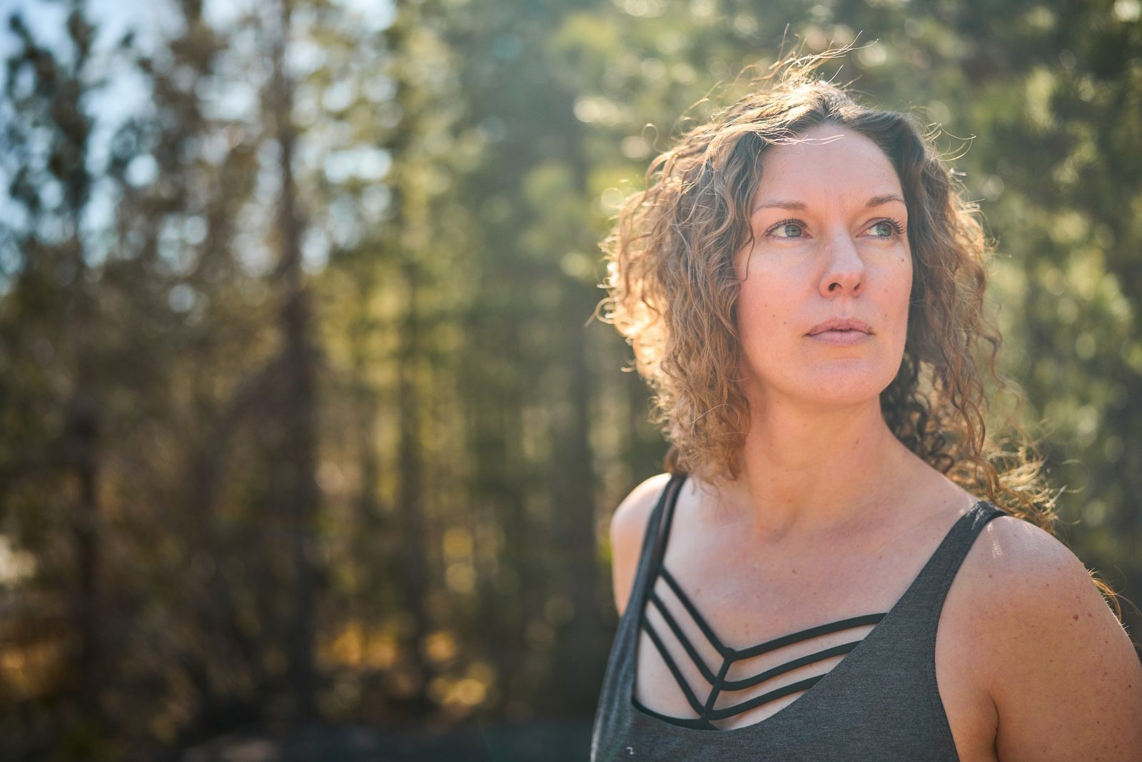 Karly Linkous outdoors among backlit pines, looking off into the distance