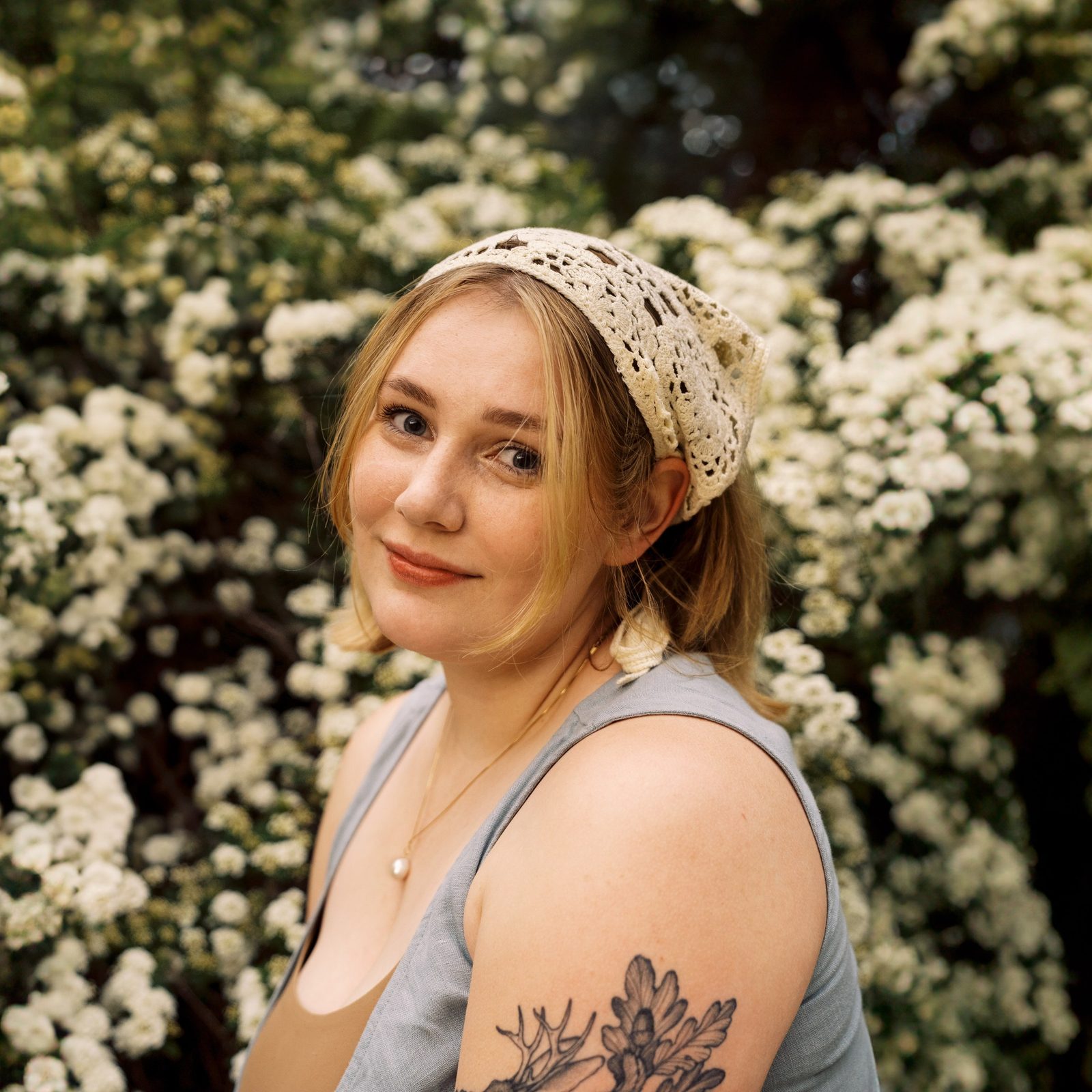 Eva Cooper in a lace headscarf, standing against a wall of white spirea blossom