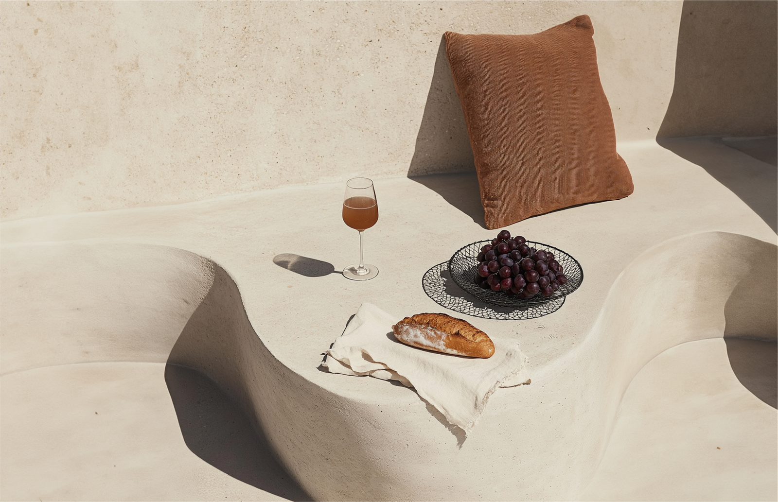 A sunlit table set with bread, grapes and a glass of wine
