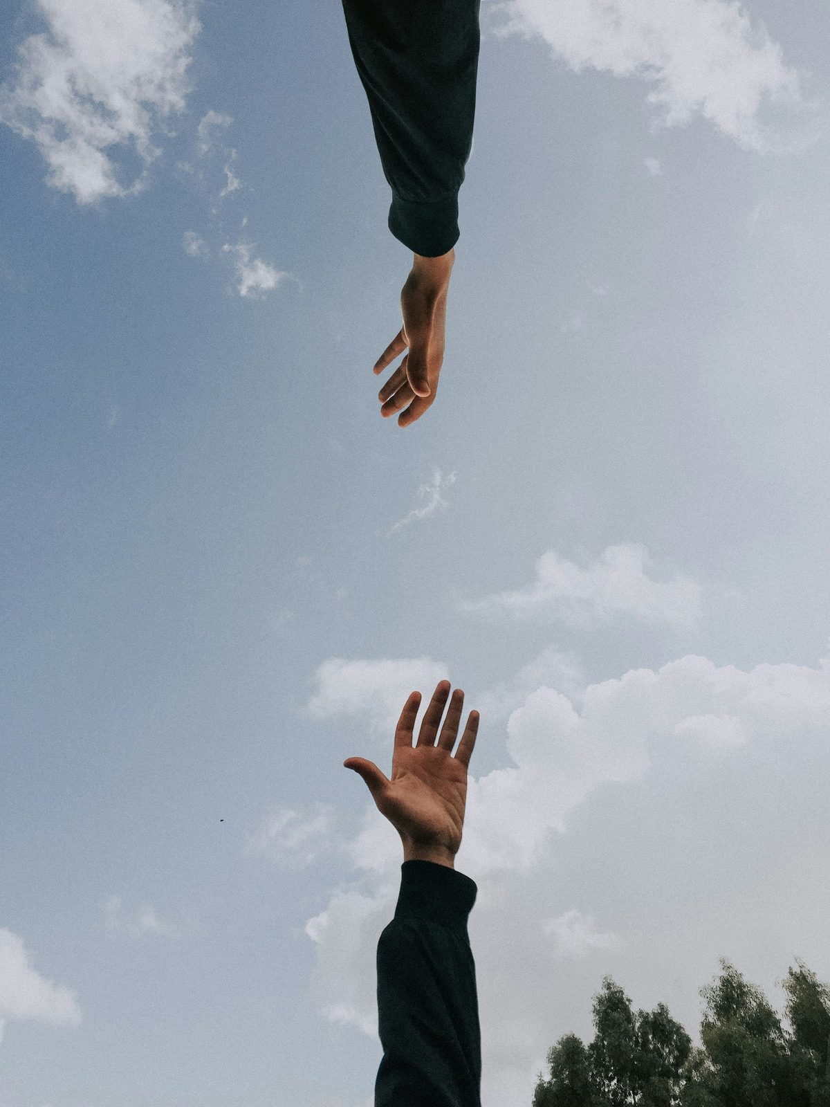 Two hands reaching towards each other against a clear blue sky