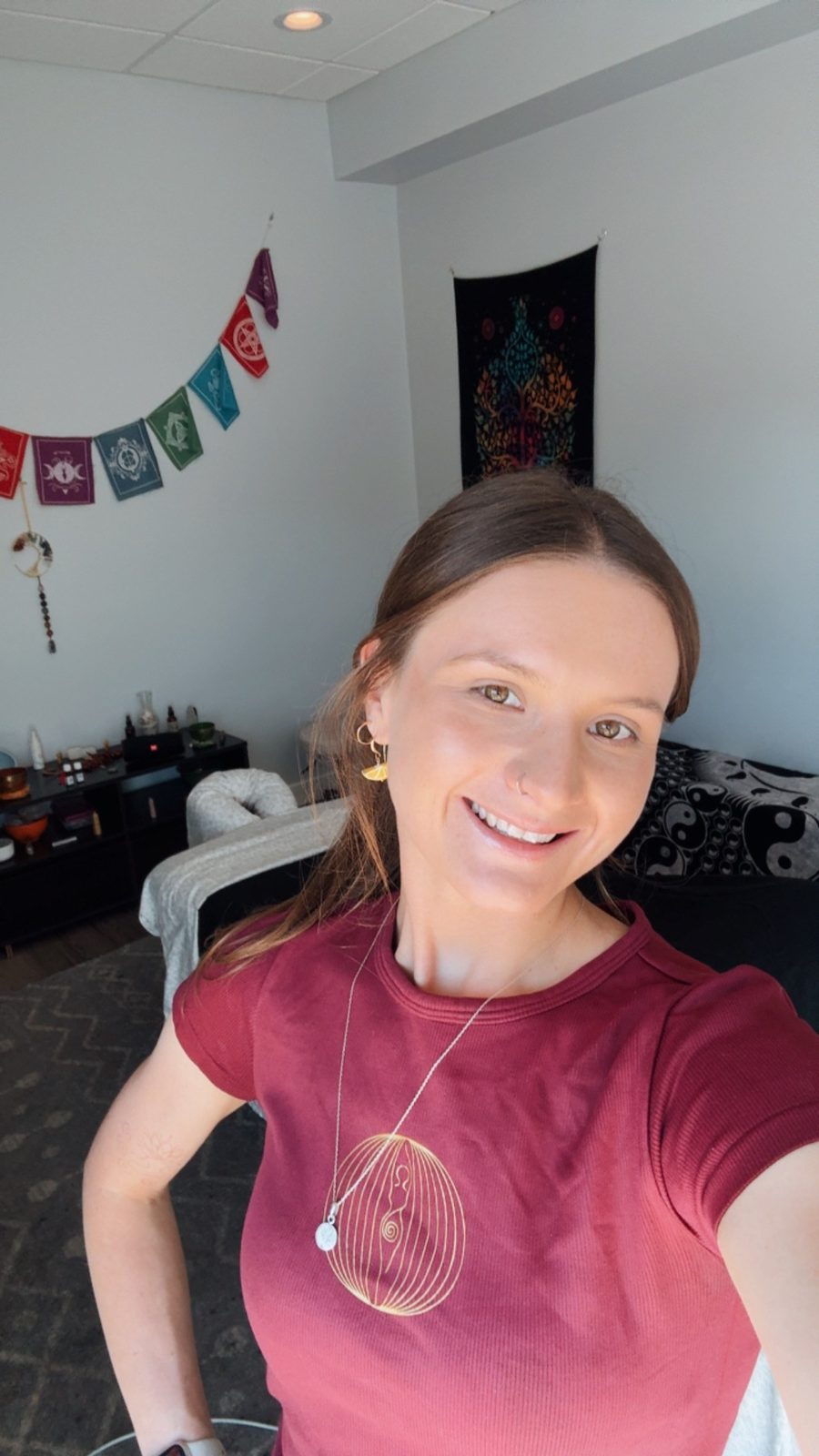Sophie Martin in her treatment room, prayer flags and a tree-of-life tapestry on the wall behind her