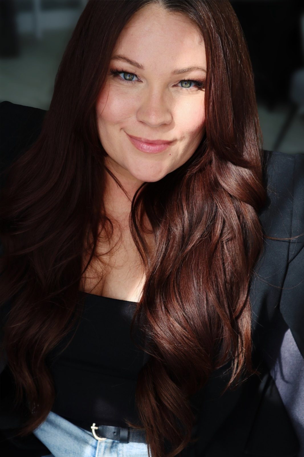 Carly Harmsen indoors, long auburn hair, in a black top and blazer